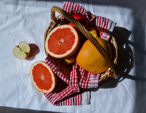 cut bright red orange grapefruit and whole in basket on white background fabric with folds in light of sun with shadows, apple