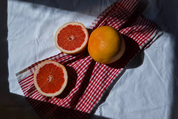 两半在白布上切下鲜红色的柚子 在阳光下 在阴影下 用褶皱剪成红色的织物 — 图库照片