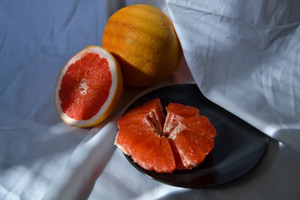 两半切碎的橙红色柚子放在盘子里 整个是白色的 有褶皱的阳光 有阴影 — 图库照片
