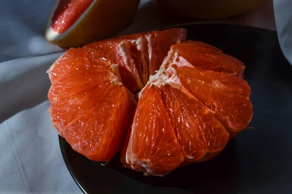 在白布上的盘子上切下鲜红色的半柚子 并在阳光下折起来 — 图库照片
