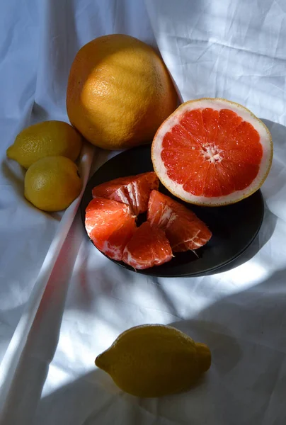 プレートの上に鮮やかな赤オレンジ色のグレープフルーツと影 柑橘系の果物と太陽の下で折り目の白い生地に黄色のレモンをカット — ストック写真