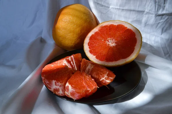 半截红橙柚子 在黑色的盘子上 白色的织物 阳光下 蓝色的阴影 — 图库照片