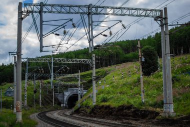 Demiryolu, yeşil dağlarda tüneli olan yollar ağaçlar, tel sütunlar, gökyüzündeki bulutlar