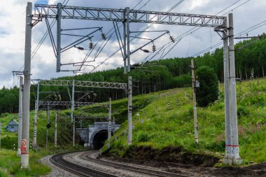 Demiryolu, yeşil dağlarda tüneli olan yollar ağaçlar, tel sütunlar, gökyüzündeki bulutlar.