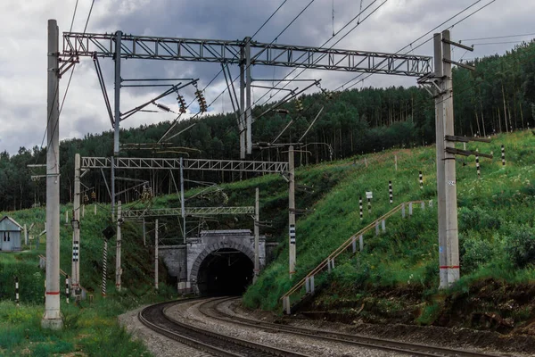 Demiryolu, yeşil dağlarda tüneli olan patika orman, tel sütunlar, gökyüzündeki bulutlar