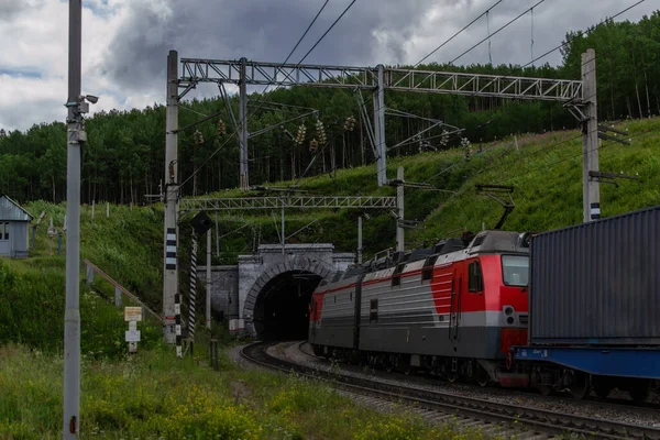 Demiryolu, kırmızı tren yeşil dağlarda bir tünelle ağaçlar, teller, gökyüzünde bulutlar
