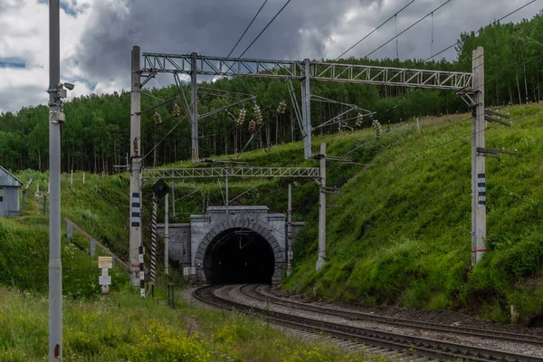 Demiryolu, yol yolu yeşil dağlarda bir tünel Ağaçlı tepeler, tel sütunlar, gökyüzünde bulutlar