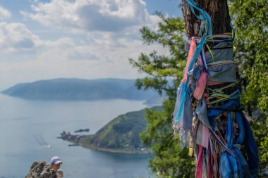 Bir ağaç gövdesindeki çok renkli kurdeleler yeşil dağların ve bulutların arasındaki mavi göl baykal manzarasının arka planına karşı.