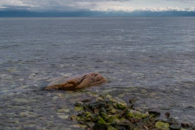 Mavi bir göl baykal 'ında, çakıl taşı kıyısında yeşil taş patika dağlar ve bulutlu gökyüzünün arka planına karşı.