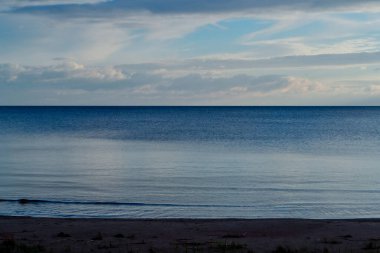 Mavi Ladoga sahilinde çimenli kumlu sahil. Gün batımında gökyüzünde bulutlarla kuzey gölünde.