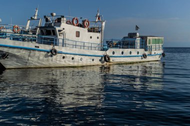 Baykal Gölü 'nün körfezinde mavi çizgili beyaz bir tekne. Güneş ışığı altında, suda yansımaları var.