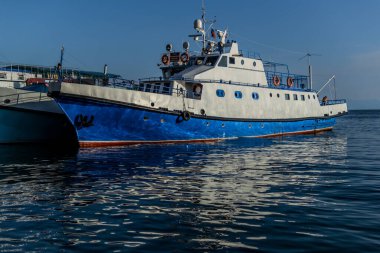 Baykal Gölü 'nün körfezindeki iskelede kırmızı çizgili beyaz mavi gemiler gün batımında suda yansıyor.