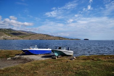 Beyazlar mavi ve gri küçük tekneler yeşil çimenli sahillerde Baykal Gölü körfezinde tepeler ve dağlar arasında, günbatımı