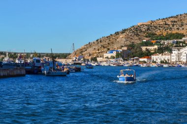 Balaklava tatil köyü boyunca uzanan mavi parlak tekne, ev ve binaların yakınlarındaki rıhtımlarda bulunan beyaz gemilerin arasında güneşli.