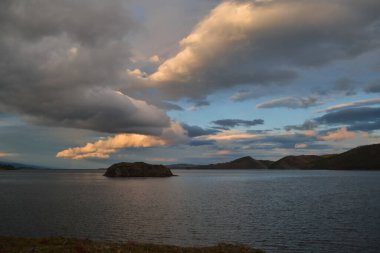 Akşam sarısı turuncu günbatımı. Baykal gölünde bulutlar, adalar ve dağlar.