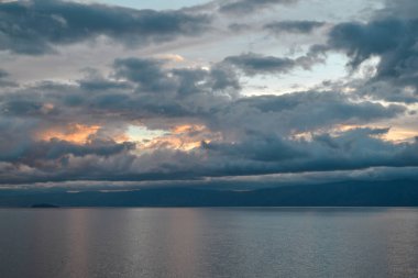 Akşamları parlak turuncu pembe günbatımı Ufukta dağ sırtlı gümüş gri mavi bulutlar Baykal Gölü üzerinde