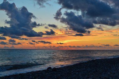 Çakıl taşlı sahil denizinde mavi bulutlu parlak turuncu pembe gün batımı.