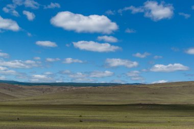 Mavi gökyüzünde beyaz, tüylü, hafif bulutlar yeşil çimen tarlası, tepeler, açık alan.