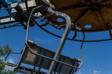 Eski teleferik yuvarlak paslı yapı gri koltuklu, güneşli mavi gökyüzü, dallar