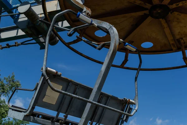 Eski teleferik yuvarlak paslı yapı gri koltuklu, güneşli mavi gökyüzü, dallar