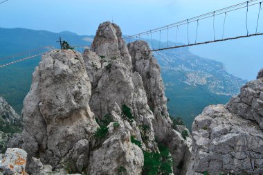 Dik kayalıklardaki uçurumun üzerinde asılı asma köprü Ai-Petri, Kırım. Karadeniz 'in zeminine karşı, güzel yaz manzarası