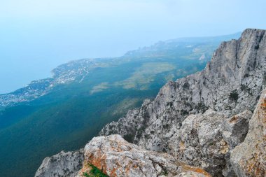 Büyük kayalık kayalıkların manzarası mavi deniz kıyısının arka planında şehir ve ormanla birlikte.