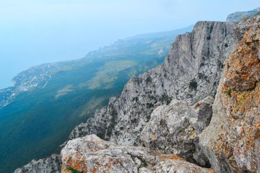 Karadeniz kıyılarının arka planında kızıl yosunlu dik kayalık uçurum, aşağıdaki şehir ve orman, yaz mevsimi