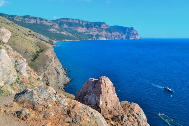 Karadeniz körfezinin güzel, taştan kıyı manzarası. Tepeler arasında gemileri ve yüksek yeşil dağları olan mavi sular. Kırım, yaz manzarası