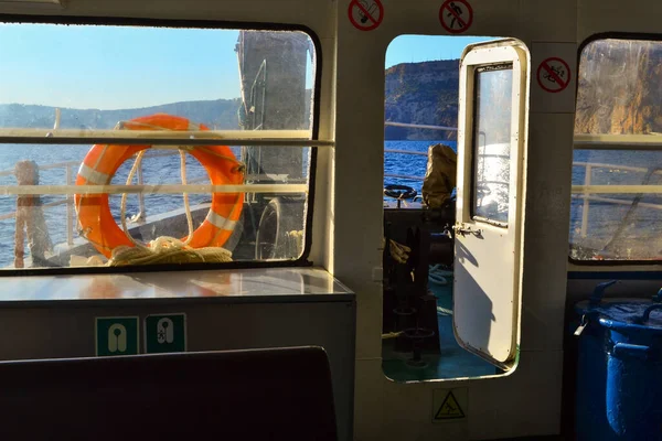 interior inside cabin of old yacht, ship with windows and red life buoy, white door in the light of sun in blue sea with rocks, mountains