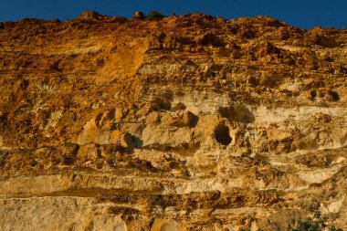 Yüksek kırmızı kumlu, kumlu, kumlu, kumlu bir uçurum. Karadeniz kıyısında günbatımının ışığında delikleri var. Güney Kırım. Mavi deniz.