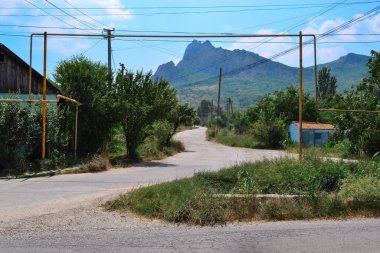Köy yolu, yüksek, keskin, mavi dağların arka planına karşı. Yaz Kırım, ağaçlar