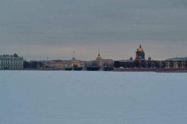 St. Petersburg 'da kış seti, temiz renkli binalar ve donmuş Neva nehrinin kıyısındaki St. Isaac Katedrali. Bulutlu gökyüzü