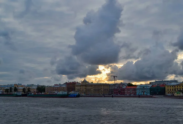 青ネヴァ川のほとりに日陰でカラフルな歴史的な家とサンクトペテルブルクの堤防 大きな積雲の間に黄色の太陽の光 — ストック写真