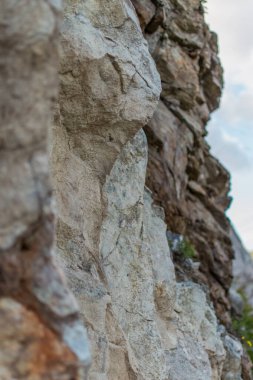 Sert taş desenli kaya, bej rengi açık kahverengi uçurum. Farklı katmanlarda levhalar. Bulutlu. Baykal Dağları