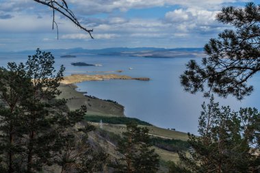 Körfez mavisi Baykal Gölü 'nün yamacında, adaları ve yarımadası olan çam ağaçlarının yeşil kozalaklı dalları. Ufuktaki dağlar. Sibirya doğa manzarası. Bulutlu gökyüzü