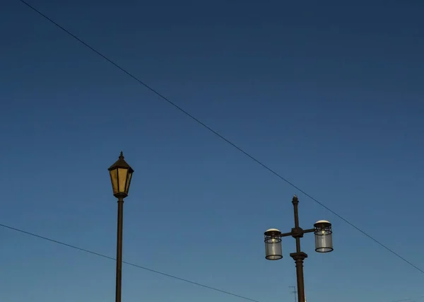古老的黑色装饰灯笼 柱子上有玻璃 阳光照射下两根杆子上的三盏路灯 蓝天渐变与铁丝网 夜路城市街道 — 图库照片
