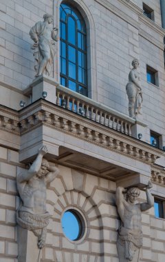 Ostrovsky Meydanı 2a, Saint Petersburg, Rusya, 11.10.2020. Antik heykel, duvarda duvarlarla örülü gri binaların balkonunda duruyor. Pencerelerde mavi gökyüzü yansıması. Atlantisliler