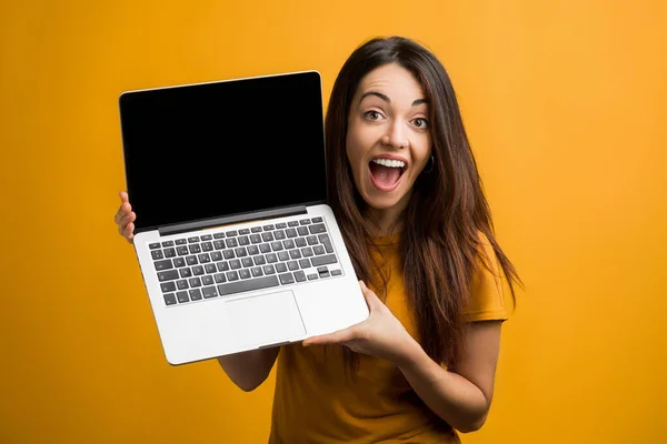 Portrait of laughing young woman with computer. Smiling caucasian girl using computer and posing on orange background.