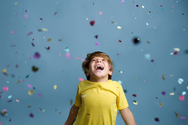 Smiling beautiful child jumping in confetti. Portrait of child on colored blue background.