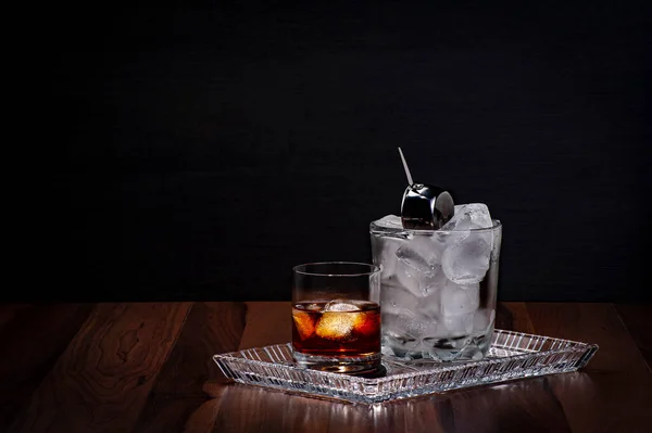 Kristal tepside servis edilen ahşap bir masanın üzerinde bir bardak viski ve bir buz kovası.