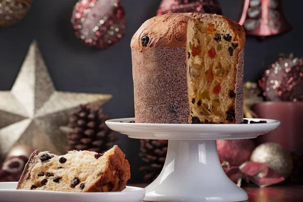 Beyaz bir tabakta panettone 'u kapatıyoruz. Kenarında bir dilim servis var. Odaklanmamış ve doymamış bir Noel süslemesi var..