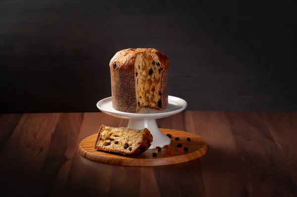 Panettone beyaz bir tabakta, yan tarafında kesik olan tahta bir masa üzerinde, soldan sağa doğru yönelen bir ışık ile merkezde, boşluğu kopyala.