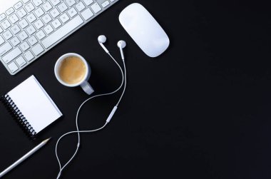 Ofis çalışma alanının en üst görüntüsü, klavyesi, kalemi, kulaklığı, faresi, defteri ve bir fincan kahvesi olan siyah masa. Kopyalama alanı ile, düz uzanır.
