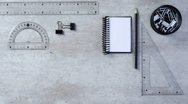 Not defteri, kalem, cetvel, pusula, kare, ataç ve iğneli bir masanın üst görünümü.