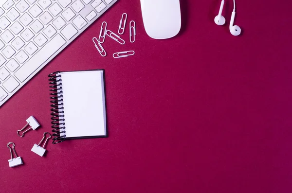 Not defteri, bilgisayar klavyesi, fare, ataç, ataç ve kulaklık olan ofis masası. Kopyalama alanı olan üst görünüm.