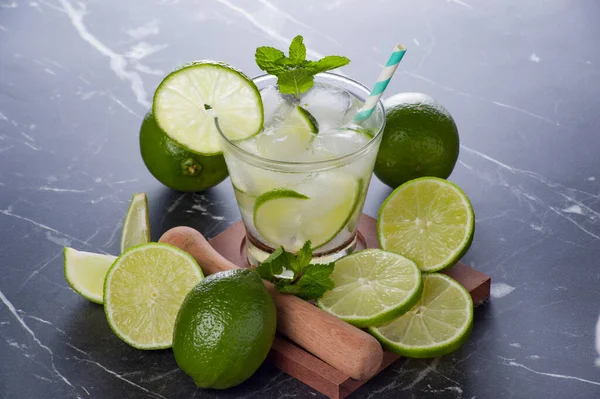 Caipirinha kokteyli mermer masada cam, limon dilimleri ve nane..