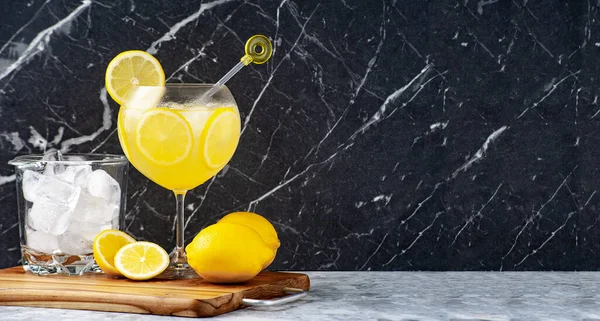 Tahta bir masanın üzerinde limon kokteyli, buz kovası, limon dilimleri, mermer arka plan. Boşluğu kopyala.