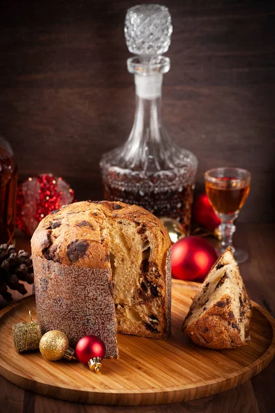 Ahşap tepside panettone dilimlenmiş. Konyak şişesi ve bir shot ile arka plan, noel baloları ve odaklanma seçin.