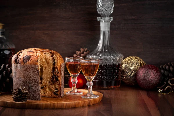 Tahta tepside panettone ve yanında iki bardak brendi. Seçici odak.