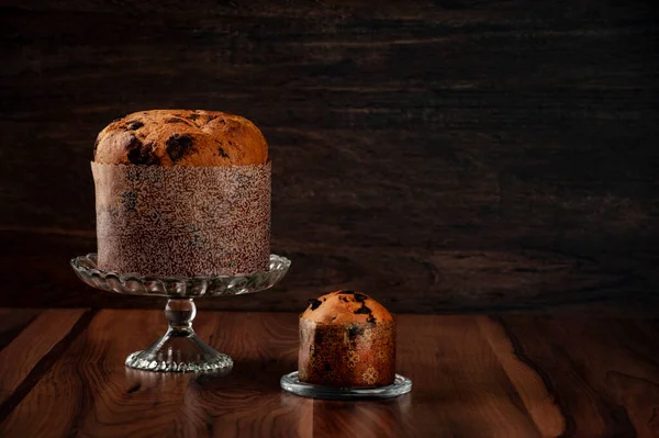 İki panettone, biri büyük diğeri de küçük, çarpıcı bir ışıkla ahşap bir masanın üzerinde. Metin için alanı olan tahta arkaplan.